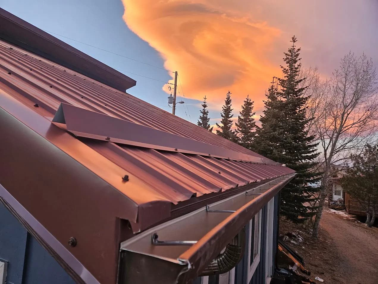 Seamless gutter on a brown metal roof at sunset